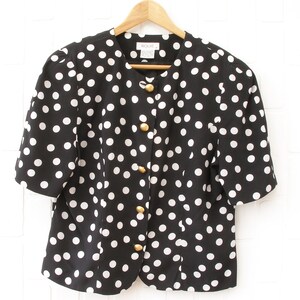 May include: A black and white polka dot button-up blouse with gold buttons. The blouse has short sleeves and a round neckline.