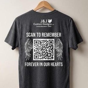 May include: A charcoal grey t-shirt with white text and graphics. The design includes a QR code, angel wings, and the phrases "SCAN TO REMEMBER" and "FOREVER IN OUR HEARTS." The shirt also displays the logo of "J&J Custom Designs LLC" from Canton/Massillon, Ohio.