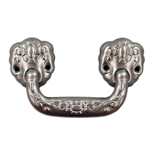 Könnte beinhalten: Silberfarbener, verzierter Zuggriff mit einem dekorativen floralen Design. Der Griff hat eine gebogene Form und zwei abgerundete Enden.
