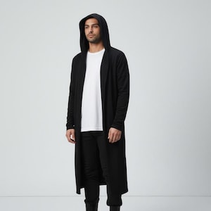 May include: A long-length black open-front cardigan featuring a hood and long sleeves, worn over a plain white t-shirt and black trousers, paired with black high-top sneakers that have prominent white rubber toe caps and thick white soles.