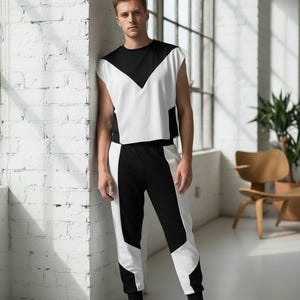 May include: A two-piece athletic outfit in black and white. The sleeveless top has a black upper section and a white lower section with a black chevron design. The matching pants are black with white panels. The person is wearing black sneakers.