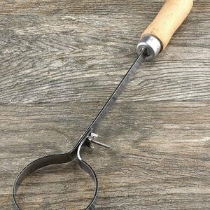 May include: A metal ring with a wooden handle attached to a long metal rod. The ring is designed to be used for lifting and moving objects.