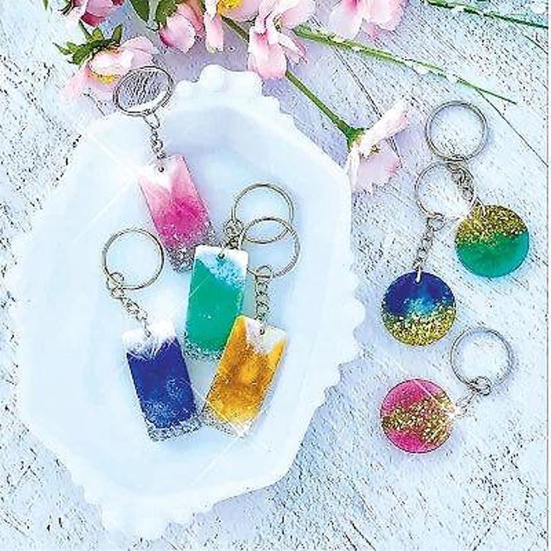 K&ouml;nnte beinhalten: Sechs bunte Schl&uuml;sselanh&auml;nger aus Harz mit Glitzerakzenten. Die Schl&uuml;sselanh&auml;nger sind rechteckig und rund. Die Schl&uuml;sselanh&auml;nger h&auml;ngen an silbernen Schl&uuml;sselringen.