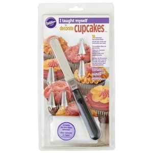 May include: A Wilton cupcake decorating set with 18 decorating ideas, tools, and instructions. The set includes a spatula, piping tips, and online video tutorials. The packaging features a colorful design with cupcakes and the text "I taught myself to decorate cupcakes".