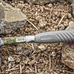 May include: A black rock pick hammer with a gray rubber grip. The hammer has a label that reads "Rock Pick Hammer".