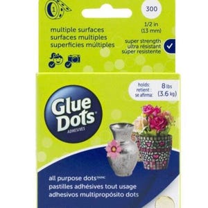 May include: A box of 300 Glue Dots adhesives, with a blue and white label that says "Glue Dots" and "All Purpose Dots". The box is yellow and has a picture of a vase and a flower pot on the front. The box also says "Holds 8 lbs (3.6 kg)".