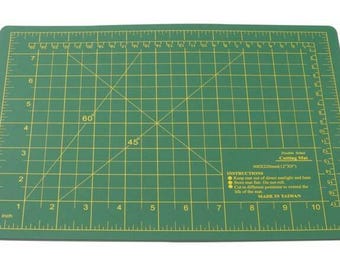 May include: Green self-healing cutting mat with a grid pattern and yellow lines. The mat has a ruler on all sides and includes instructions for use. It is labeled "Self Healing Cutting Mat" and "Made in Taiwan".