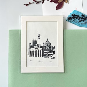 Könnte beinhalten: Schwarz-Weiß-Druck mit Berliner Wahrzeichen, darunter das Brandenburger Tor und eine Kirche. Der Druck befindet sich in einem weißen Rahmen und wird von einer transparenten Kunststoffhülle geschützt. Der Druck ist mit "Berlin" beschriftet und datiert 2019.