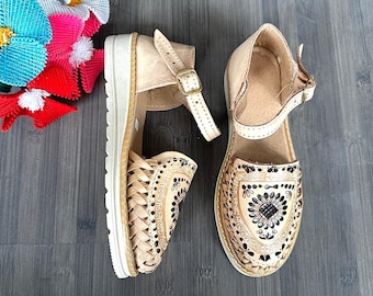 May include: A pair of tan leather sandals with black floral embroidery and an ankle strap. The sandals have a platform sole.