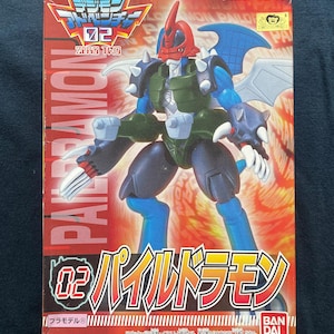 May include: A red, blue, and green plastic action figure of a dragon-like creature with wings. The figure is from the Digimon franchise and is labeled "02 PailDramon".