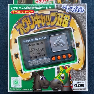 May include: A green and gold box with a silver and green handheld electronic game. The game is called "Pocket Breeder" and features a horse on the screen. The box also has the text "Oguri Cap II" and "Takara" on it.
