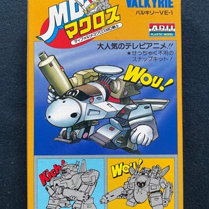 Puede incluir: Una caja para un kit de maquetas de plástico del MD Valkyrie, un robot de la serie de anime Macross. La caja presenta una ilustración colorida del robot, junto con el texto "Defo-Macross MD Valkyrie VE-1".