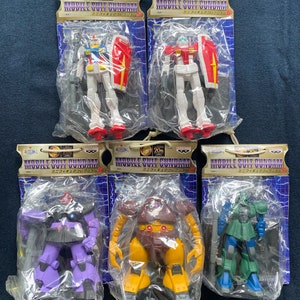 Könnte beinhalten: Fünf verpackte Mobile Suit Gundam Miniaturfiguren-Sammlungsspielzeuge. Die Figuren sind in verschiedenen Farben, darunter Weiß, Rot, Blau, Lila, Braun und Grün. Jede Figur befindet sich in einer transparenten Plastikverpackung mit einem Kartonheader mit japanischem Text.