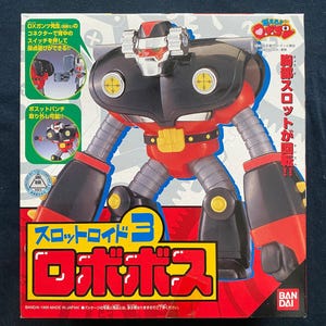 Puede incluir: Un juguete robot rojo, negro y amarillo con un compartimento de pecho giratorio. El juguete es parte de la serie "Slotroid 3" y está etiquetado como "Robopos".