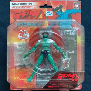 May include: A green action figure of a superhero with a red and blue costume, standing on a red and black background. The figure is packaged in a clear plastic blister pack with a red and black cardboard backing. The packaging features the text "Microman Micro Action Series MA-09 Devilman (TV Anime Version)" and a logo for "Toy's Dream Project Limited Edition".