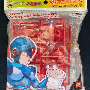 Puede incluir: Un kit de modelo de plástico de un personaje robot rojo de la serie de videojuegos Mega Man X. El kit incluye una variedad de piezas, incluyendo la cabeza, los brazos, las piernas y las armas del robot. El empaque presenta una imagen de dibujos animados del robot y el texto "System Up Armor Series Spinning Blade (Red)".
