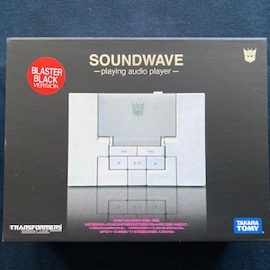 May include: A black box featuring a Soundwave audio player, with the text "SOUNDWAVE - playing audio player -" and "BLASTER BLACK VERSION". The box has a silver and white design with the Transformers logo and the Takara Tomy logo.