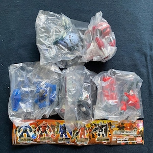 May include: A collection of unopened miniature robot figures in clear plastic packaging. The robots are various colors, including red, blue, and black. A colorful promotional card with robot illustrations is visible.