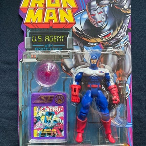 K&ouml;nnte beinhalten: Eine Plastik-Actionfigur von U.S. Agent aus Marvel Comics. Die Figur tr&auml;gt ein rot-wei&szlig;-blaues Kost&uuml;m mit einem rot-wei&szlig;en Schild am linken Arm. Die Figur ist in einer Plastik-Blisterverpackung mit einem violetten Projektilschild verpackt.