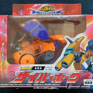 May include: A toy robot in orange, blue, and gold colors in its vehicle mode. The robot is a motorcycle with a large orange wheel and a blue wing. The packaging is in Japanese and includes the text "MC-05" and "サイクロン".
