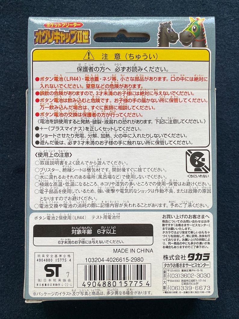 May include: A close-up of a toy horse with a red and white racing saddle. The toy is made of plastic and has a bright, colorful design. The packaging includes a warning label in Japanese, indicating that the toy is for ages 6 and up. The packaging also includes a safety warning about the use of batteries.