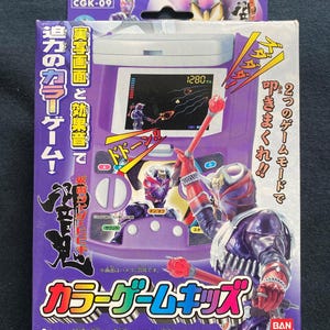 May include: A purple and white Color Game Kids box featuring a video game console design. The box has Japanese text and illustrations of a character with a red and black costume. The game screen shows a pixelated game.