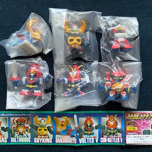 Puede incluir: Un conjunto de 8 pequeñas figuras de acción de plástico en bolsas de plástico individuales. Las figuras son todas robots con diferentes colores y diseños. Las figuras son de las series de anime Voltes V y Combattler V. Las bolsas están etiquetadas con los nombres de los robots en japonés e inglés. El texto en la parte inferior de la imagen dice "Albegas, Daltanious, Guyking, Daikumaryu, Voltes V, Com-Battler V, 全6種, 株式会社バンダイ, ベンダー 0-4111-41, BAN DAI".