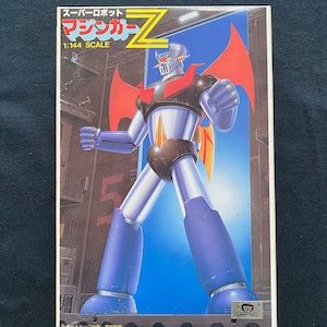 May include: A boxed 1:144 scale model kit of Mazinger Z, a Japanese super robot. The box art features the robot in a dynamic pose, with a blue, red, and silver color scheme. The background shows a cityscape.