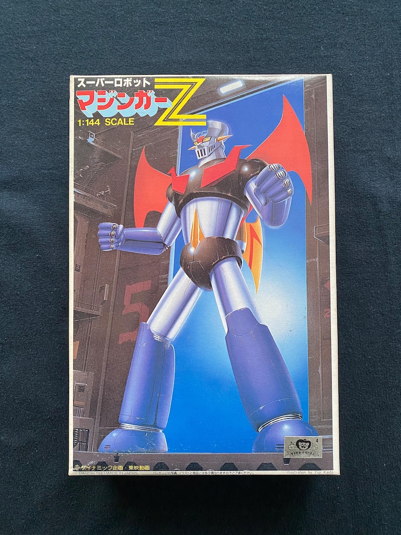 May include: A boxed 1:144 scale model kit of Mazinger Z, a Japanese super robot. The box art features the robot in a dynamic pose, with a blue, red, and silver color scheme. The background shows a cityscape.