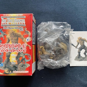 Peut inclure: Une boîte rouge avec du texte japonais et des illustrations de créatures fantastiques de la Ray Harryhausen Film Library. Un sac en plastique contient des figurines et une carte montre une figurine tenant une arme.