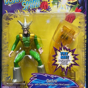 May include: A green and gold action figure of Electro from the Spider-Man comics. The figure is holding a yellow and gold arm cannon. The packaging features a yellow background with the text "Electro Spark" and "Try Me! Real Spark'n Action! See Back Panel".