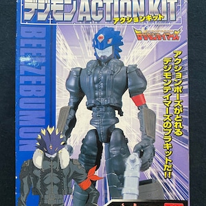 Peut inclure: Une figurine d'action bleue et noire d'un personnage Digimon, Beelzebumon, de la série animée Digimon Tamers. La figurine tient un pistolet et porte un foulard rouge autour du cou. La boîte est bleue et porte le logo Digimon Tamers.
