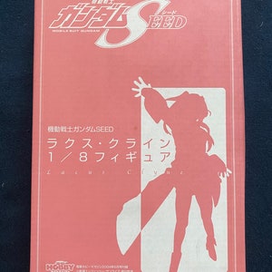 Może przedstawiać: Różowe pudełko z białym obrazkiem postaci anime. Na pudełku widnieje napis "Mobile Suit Gundam SEED" i "Lacus Clyne 1/8 Figure".