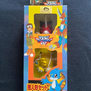May include: A yellow box with a Digimon Adventure 02 Zero Two logo. The box features a red and black Digimon character with a yellow Digimon character in the background. The text on the box reads "Digimon Adventure 02 Zero Two" and "Human Evolution Set".