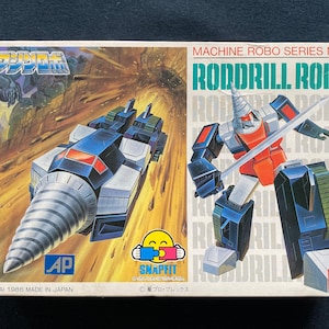 May include: Vintage Machine Robo Series No. 2 Roddrill Robo toy box. The box features a drill-shaped vehicle and a robot figure with a sword. The box has the text "BANDAI 1986 MADE IN JAPAN" and the Snapfit logo.