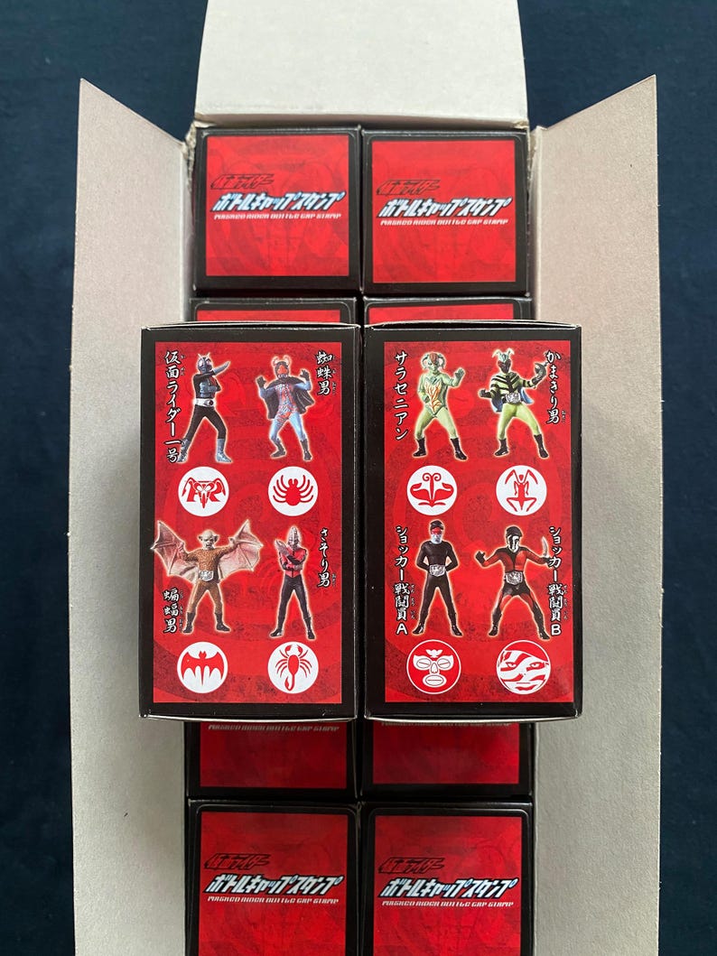 May include: Stacked boxes with red and black packaging. Each box features illustrations of various characters in action poses. The boxes are labeled with Japanese text and character names. The overall theme is action figures or collectibles.