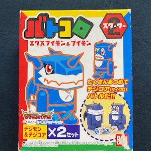 Peut inclure: Une boîte bleue et jaune avec une image d'un personnage de dessin animé bleu et blanc sur le devant. La boîte est étiquetée "Digimon" et "Starter 2". La boîte contient également une image de deux dés bleus et blancs.