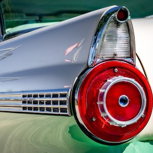 May include: Close-up of a classic car's tail light. The tail light is a vibrant red with a chrome bezel and a clear lens. The car's body is a light cream color with chrome trim. The image highlights the vintage design of the vehicle.