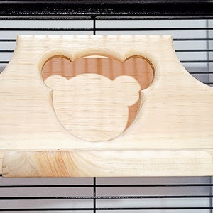 Puede incluir: Un estante de madera con un recorte en forma de cabeza de oso. El estante est&aacute; dise&ntilde;ado para encajar dentro de una jaula.