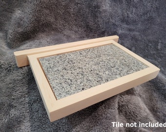 Puede incluir: Un marco de madera con un inserto de baldosa de granito gris claro. El marco está hecho de madera natural y tiene un diseño simple y elegante. Baldosa no incluida.