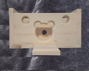 Puede incluir: Un juguete de madera con un recorte en forma de oso y dos agujeros redondos. El juguete está hecho de madera natural y tiene un color marrón claro.