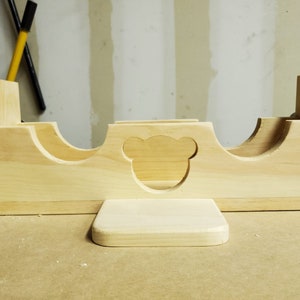 Puede incluir: Un organizador de juguetes de madera con tres compartimentos y un recorte en forma de oso. El organizador tiene una peque&ntilde;a plataforma en la parte delantera.