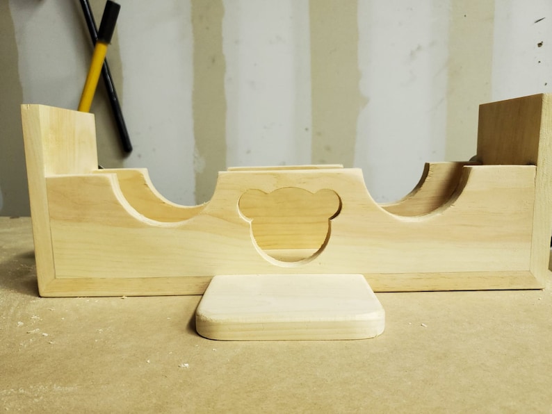 Puede incluir: Un organizador de juguetes de madera con tres compartimentos y un recorte en forma de oso. El organizador tiene una peque&ntilde;a plataforma en la parte delantera.