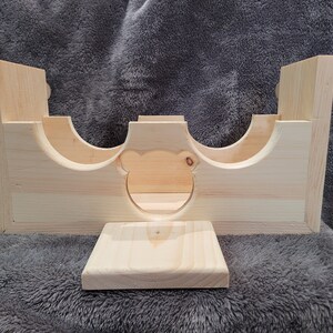 Puede incluir: Una casita de madera para animales peque&ntilde;os, con una abertura en forma de oso y una plataforma separada. La casita est&aacute; hecha de madera natural sin terminar.