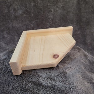 May include: A natural wood corner shelf, unfinished and ready to be stained or painted. The shelf is made of solid wood and has a simple, modern design.