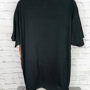 Może przedstawiać: Gładki czarny t-shirt z kr&oacute;tkim rękawem na manekinie. Odzież ma gładki tył z okrągłym dekoltem i standardowym obszyciem, z widocznym fragmentem graficznego nadruku na bocznym panelu koszulki.