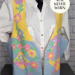 May include: A sleeveless vest featuring a yellow striped upper section and a light blue checkered lower section, adorned with colorful floral and geometric quilt-style appliqués. A circular white tag displays the text NEW NEVER WORN.