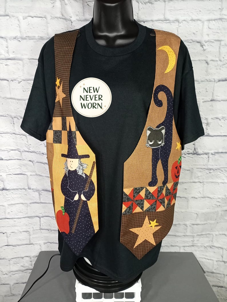 Może przedstawiać: Czarny t-shirt noszony pod bezrękawnikiem z motywem Halloween. Kamizelka przedstawia czarownicę, czarnego kota, p&oacute;łksiężyc, gwiazdy i dynię. Okrągła naklejka na t-shircie zawiera napis NEW NEVER WORN czarnymi literami.