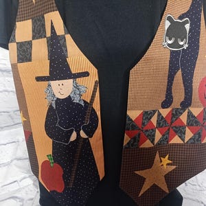 Może przedstawiać: Kamizelka bez rękaw&oacute;w z patchworkowym wzorem z motywami Halloween. Tkanina przedstawia czarownicę z miotłą, czarnego kota, czerwone jabłko i ż&oacute;łte gwiazdy na beżowym, brązowym i czarnym tle, założona na czarną koszulkę.