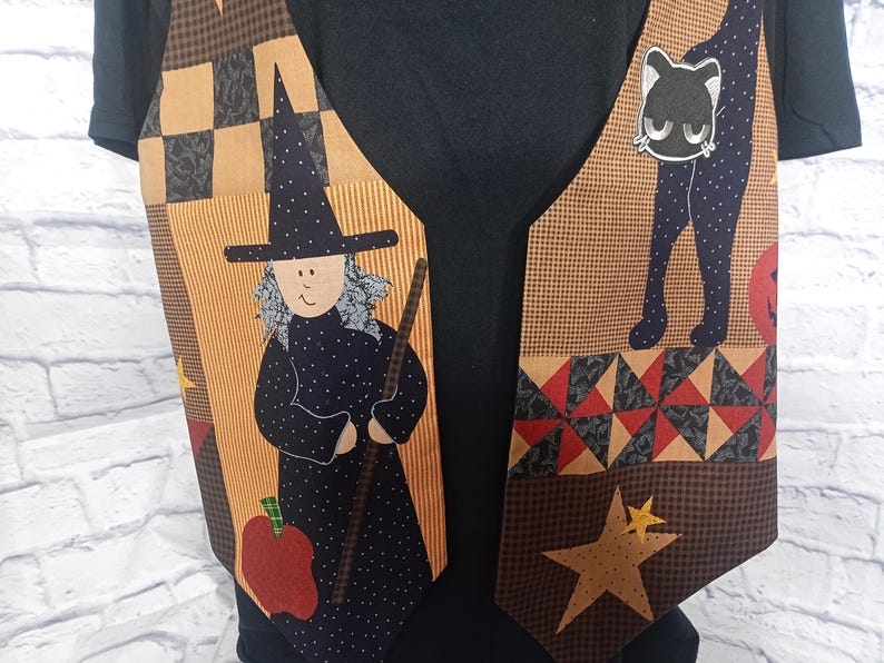 Może przedstawiać: Kamizelka bez rękaw&oacute;w z patchworkowym wzorem z motywami Halloween. Tkanina przedstawia czarownicę z miotłą, czarnego kota, czerwone jabłko i ż&oacute;łte gwiazdy na beżowym, brązowym i czarnym tle, założona na czarną koszulkę.